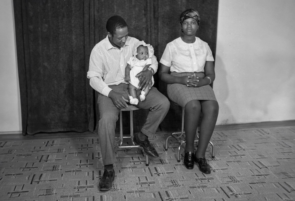 Woman in a headscarf seated next to man in western clothing holding an infant, photographed in Mr. M.T. Ramakatane's City Centre Studio. Ramakatane Archive 7, 1968.